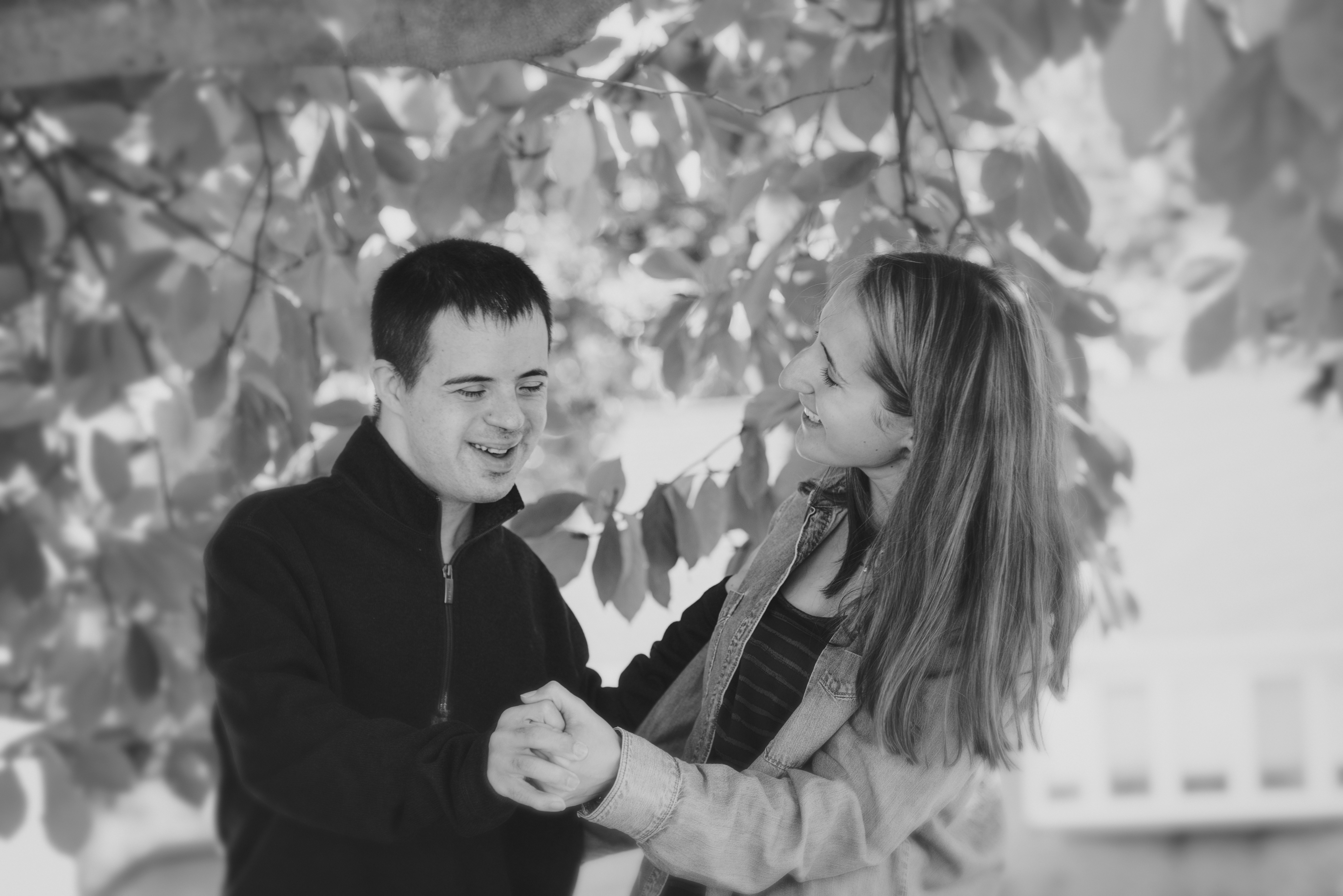 This black-and-white photo shows two people from the waist up. They are holding hands in a way that suggests they are dancing.